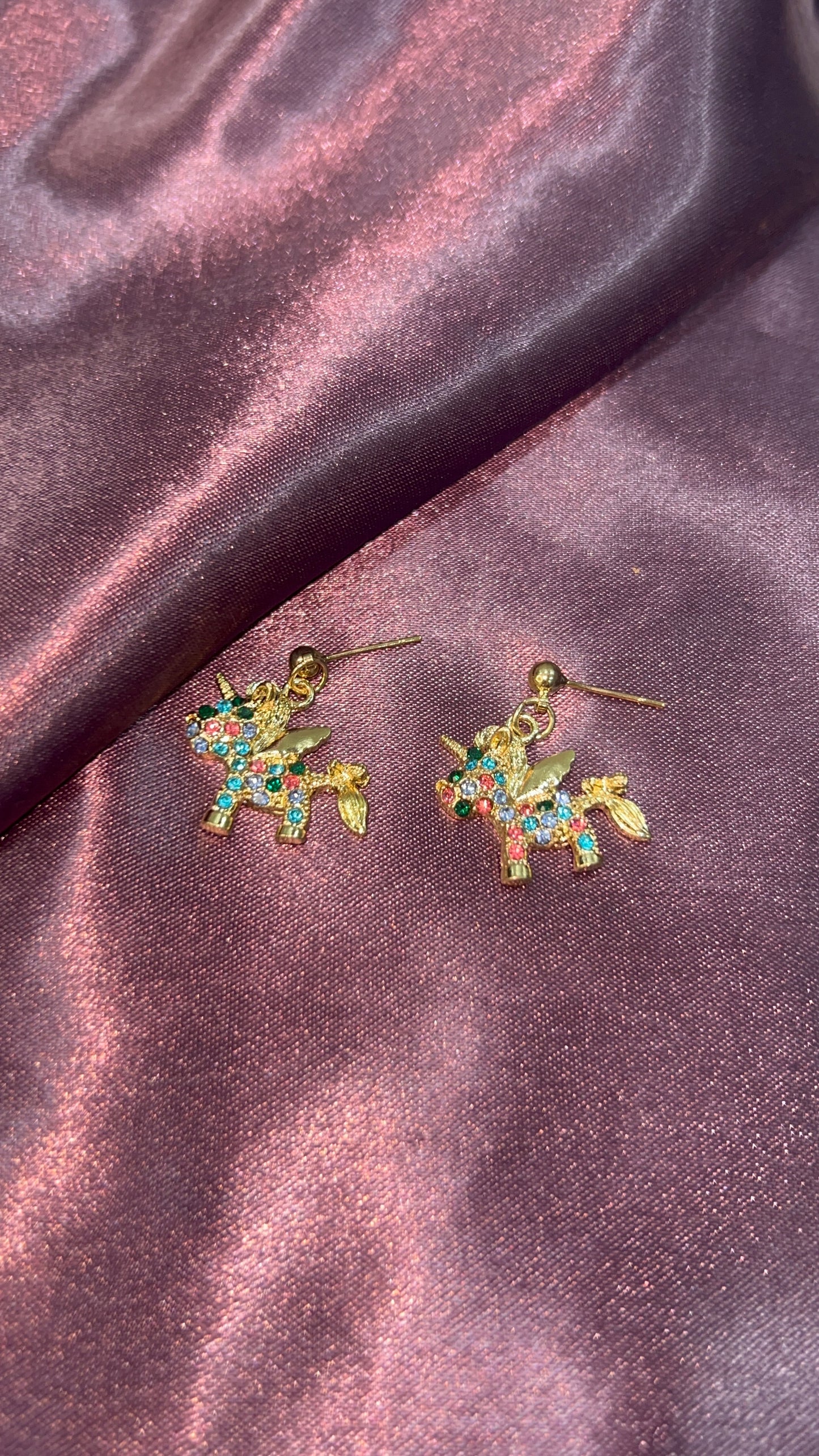 Unicorn-shaped earrings on a satin surface