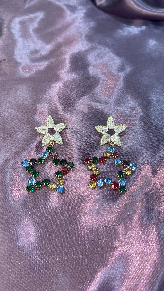Star-shaped earrings with multicolored gemstones on a marbled purple surface