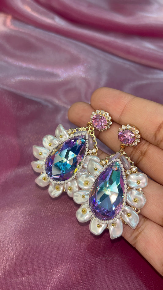 Earrings with colorful gemstones held against a pink fabric background