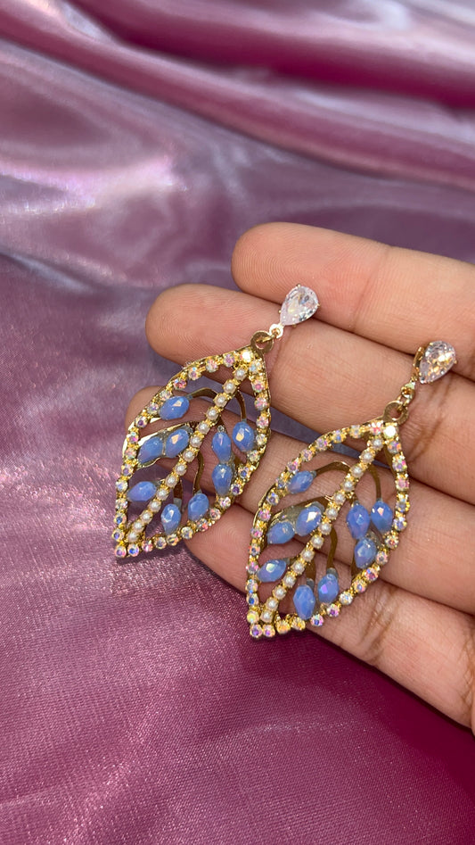 Gold earrings with blue stones held by a hand on a pink fabric background