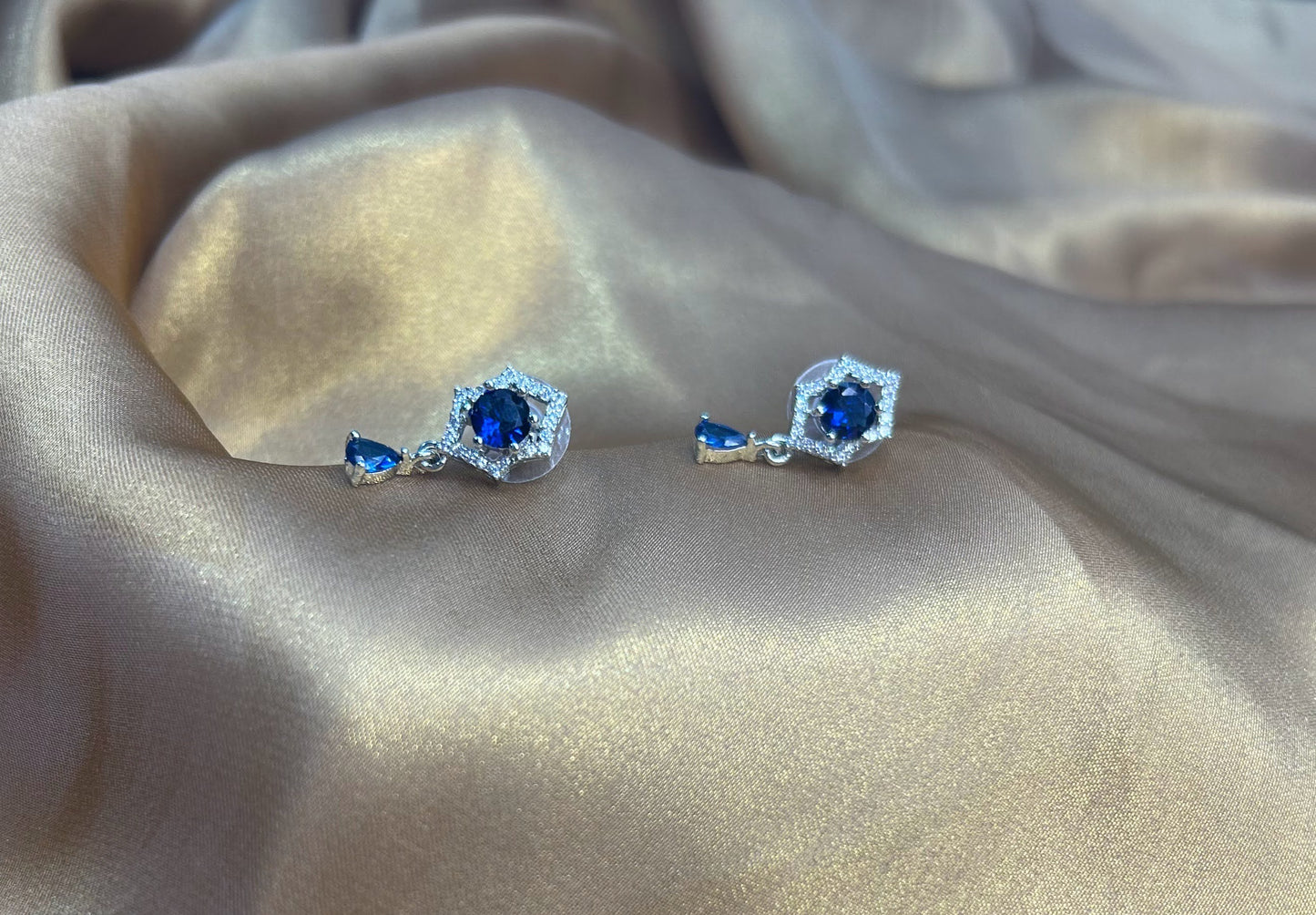 Pair of silver earrings with blue gemstones on a beige fabric background