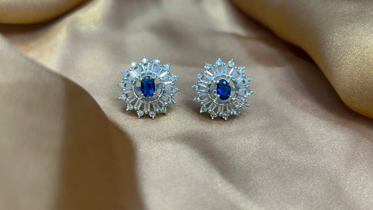 Pair of silver earrings with blue gemstones on a beige fabric background
