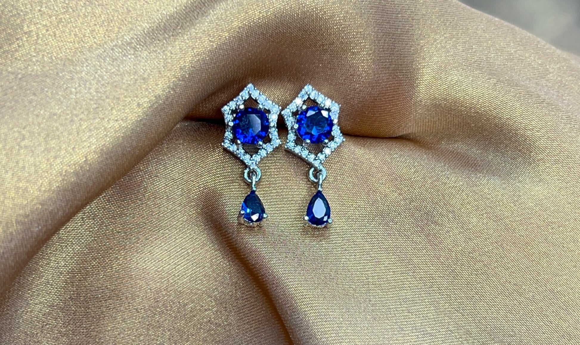 Pair of earrings with blue gemstones on a beige fabric background