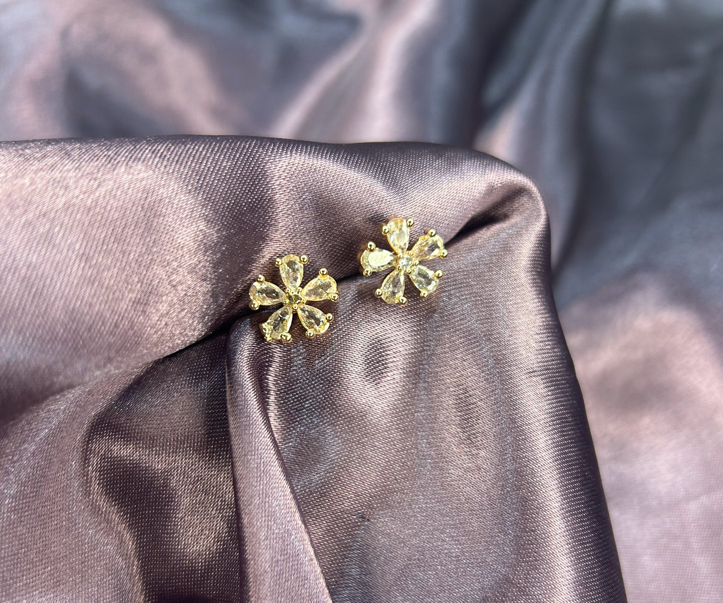 Pair of gold floral earrings on a textured gray fabric background