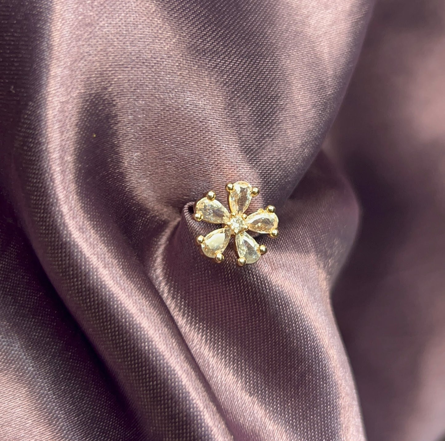 Gold flower-shaped earring on a purple fabric background
