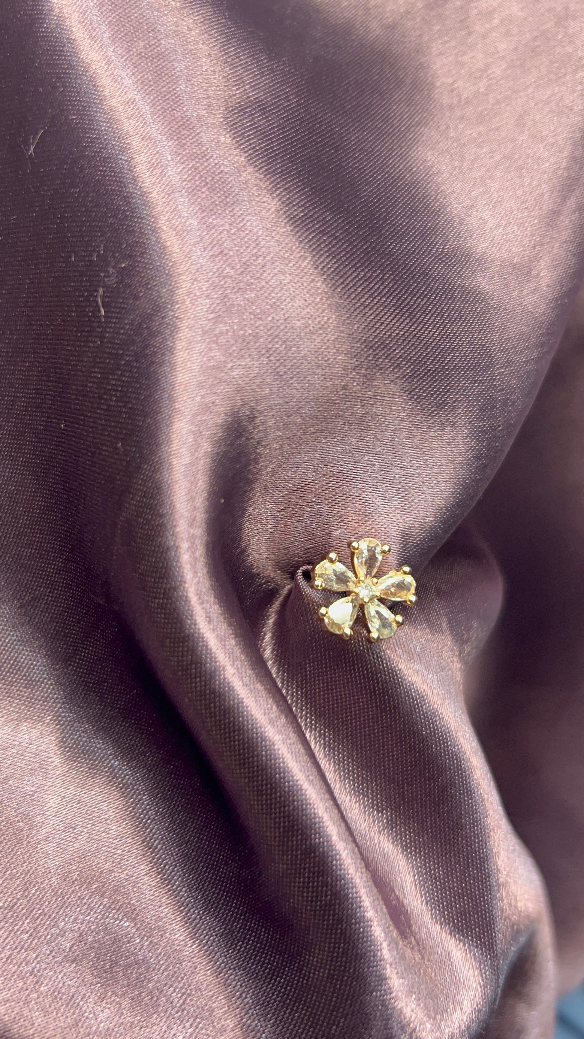 Gold flower-shaped earring on a textured fabric surface