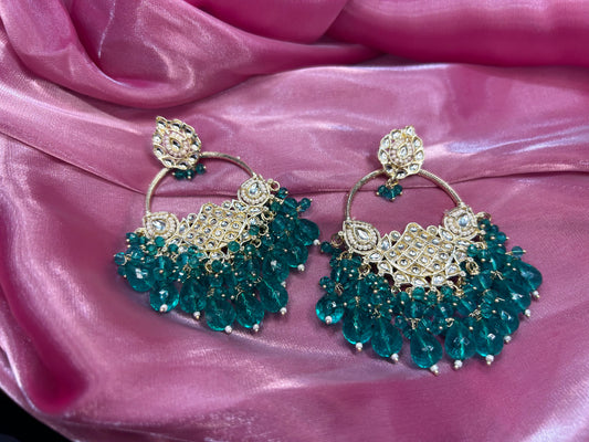 Pair of teal and gold earrings on a pink fabric background