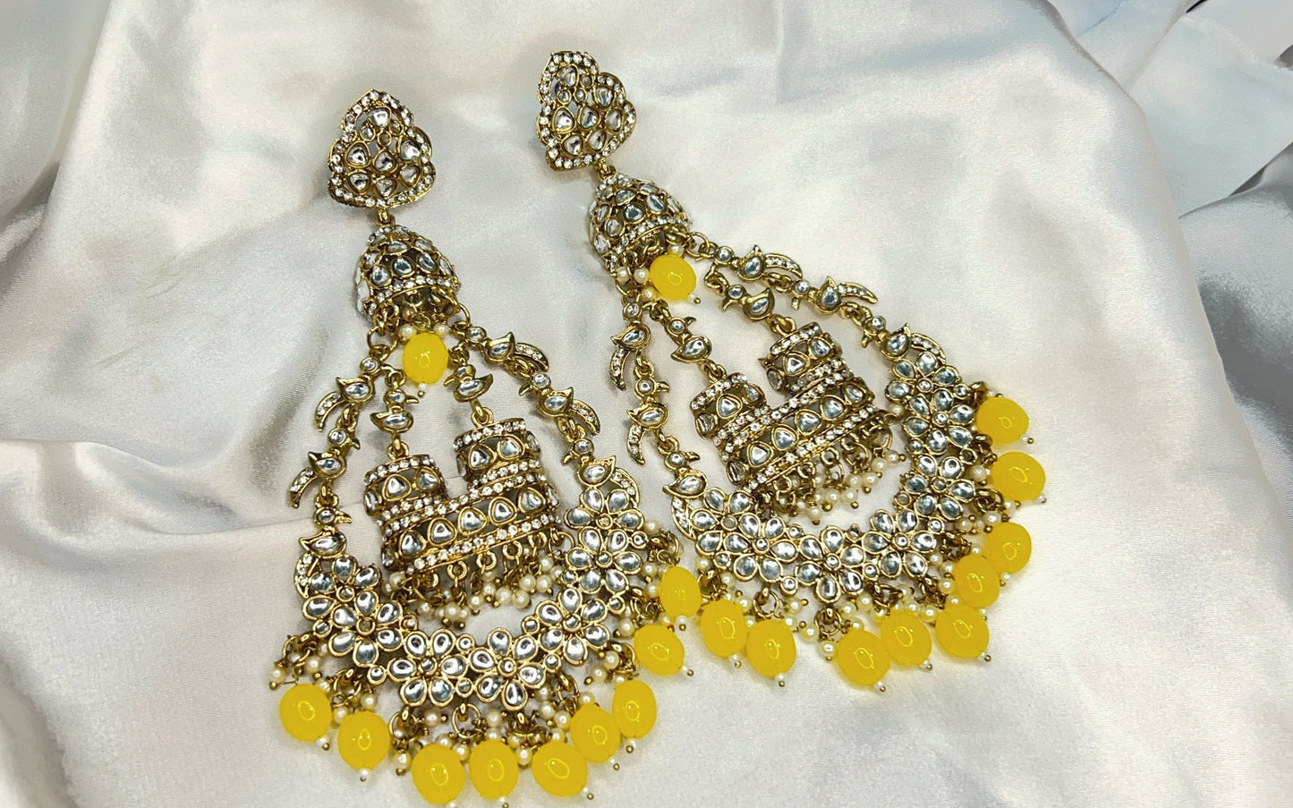 Pair of ornate earrings with yellow beads on a white fabric background