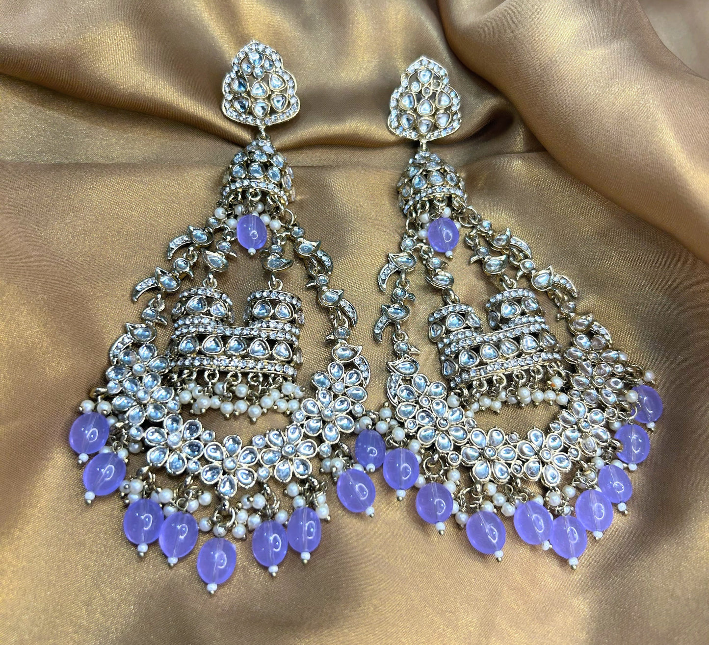 Ornate silver earrings with purple stones on a gold fabric background