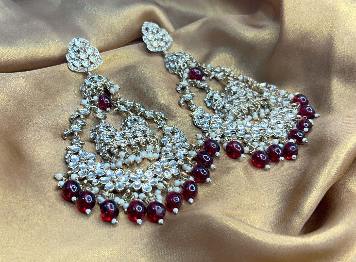 Ornate earrings with red gemstones on a beige fabric background
