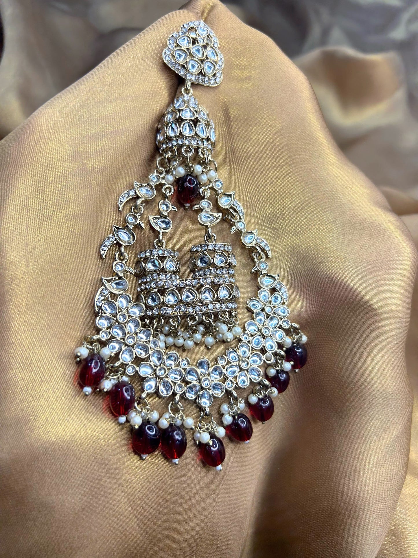 Ornate silver and red gemstone earring on a beige fabric background