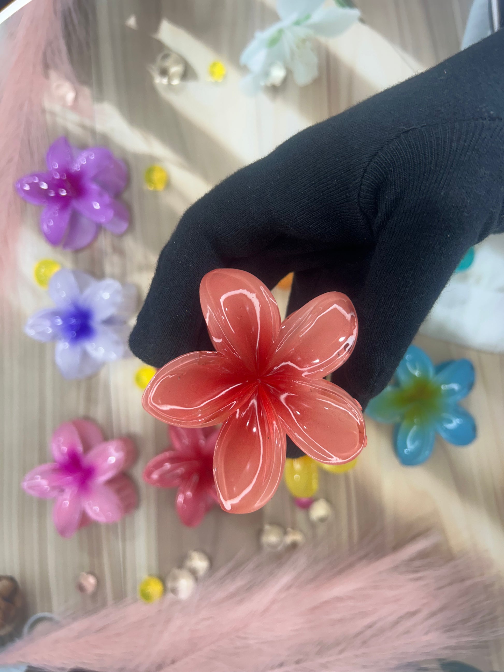 Red flower-shaped object held by a gloved hand with colorful flowers in the background.