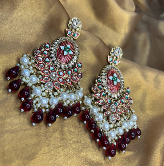 Ornate earrings with red, white, and gold colors on a satin background