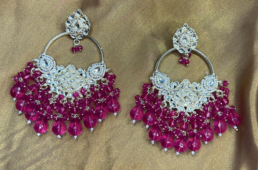 Pair of ornate earrings with pink beads on a brown fabric background