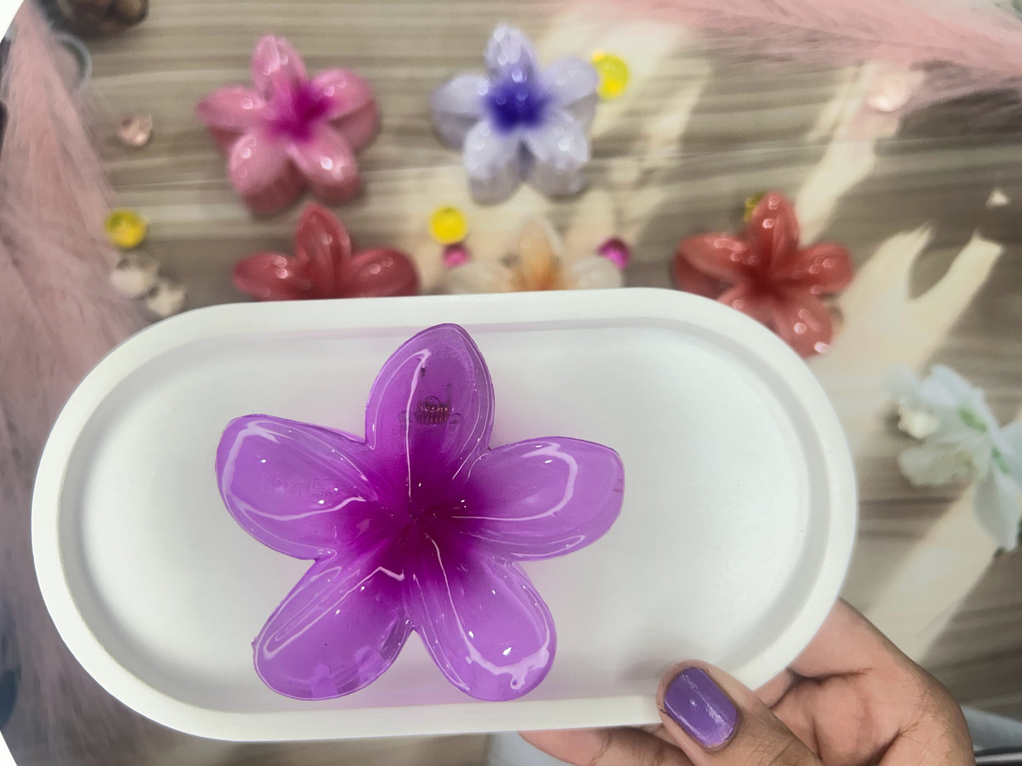 Purple flower-shaped object on a white base held by a hand with purple nail polish.