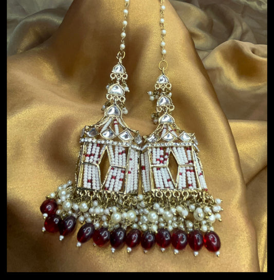 Ornate earrings with red and white beads on a gold fabric background