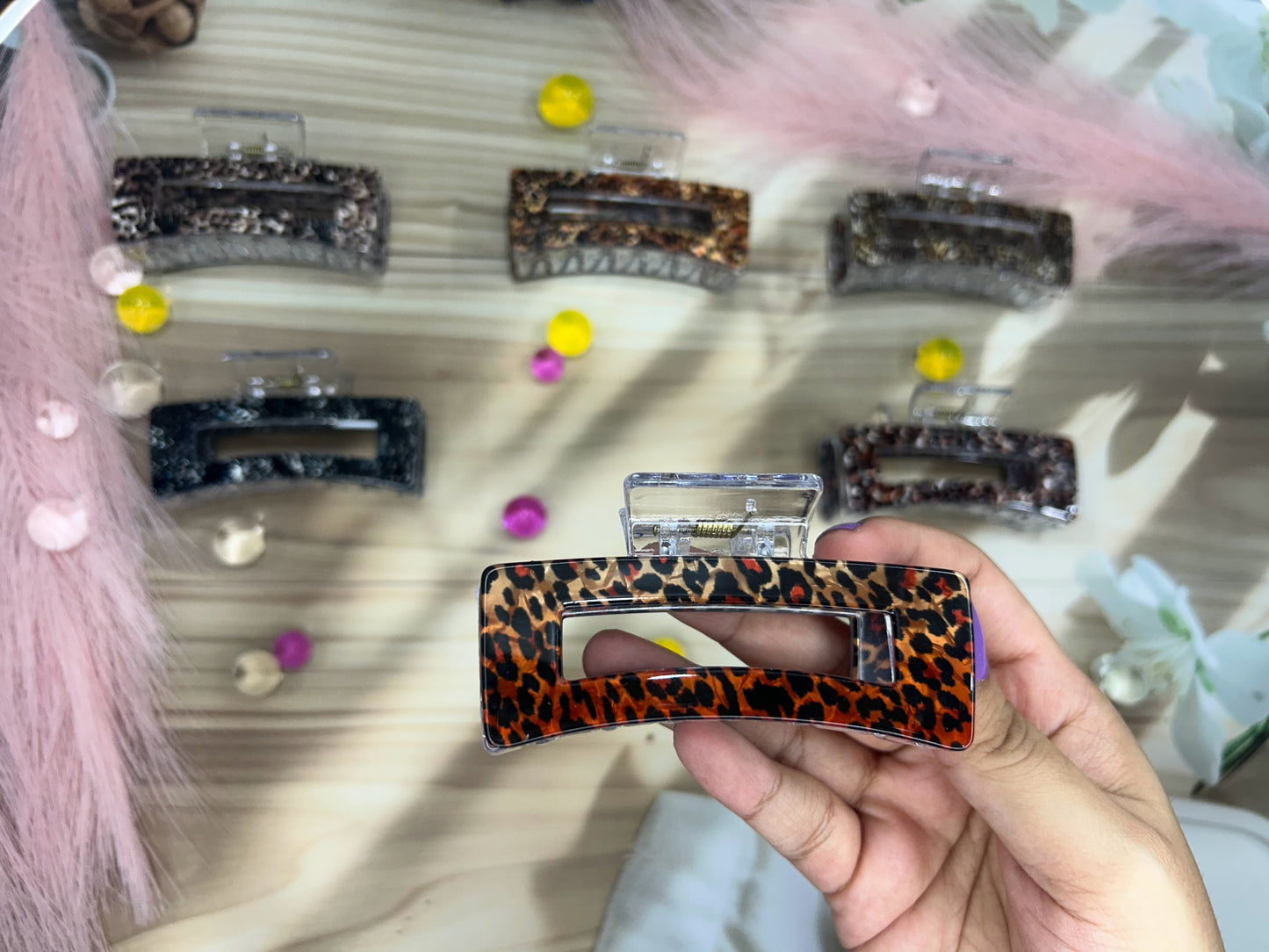 Hand holding a leopard print hair clip with more clips in the background on a textured surface.