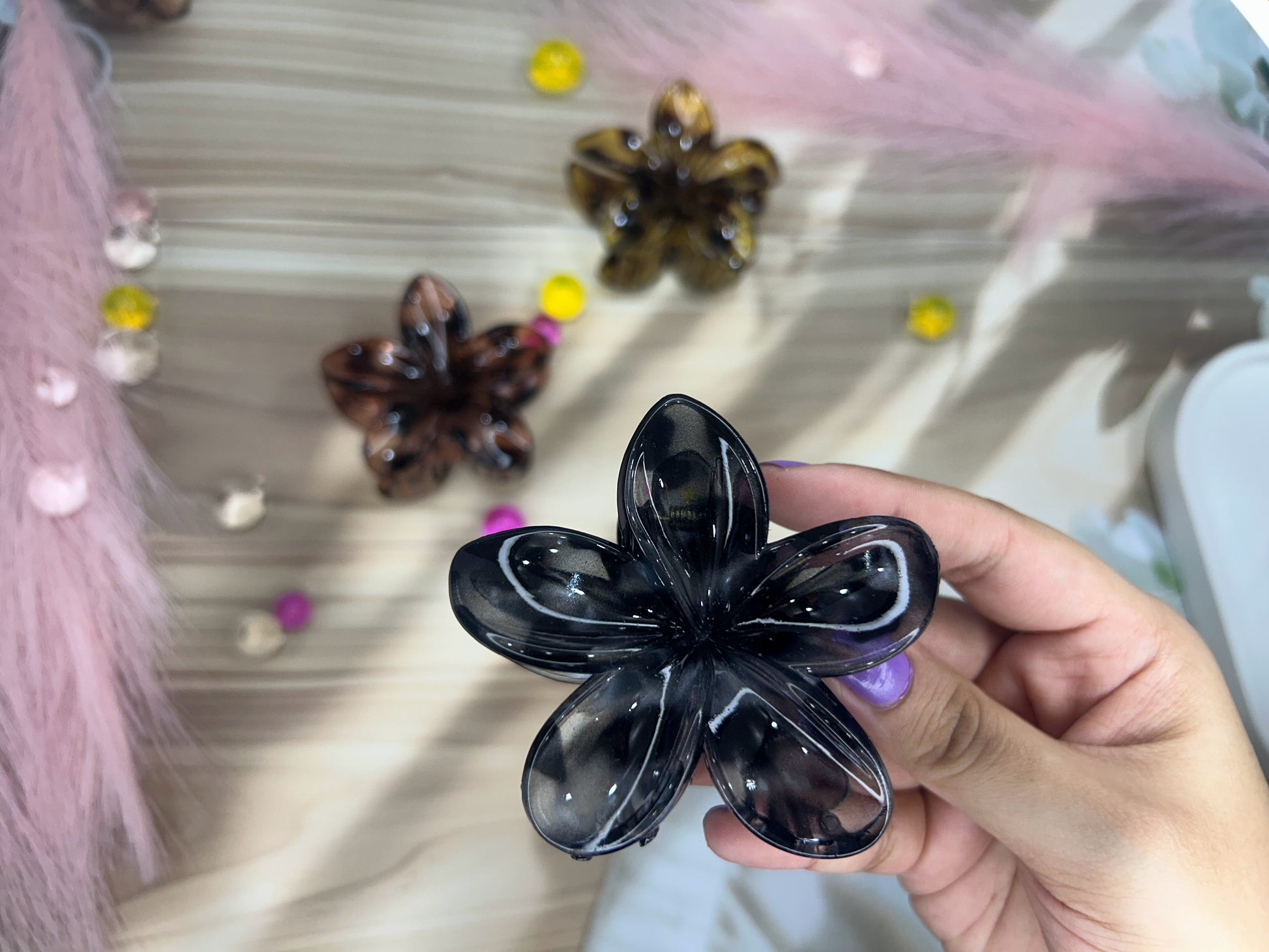 Black flower-shaped hair clip held by a hand with blurred decorative background