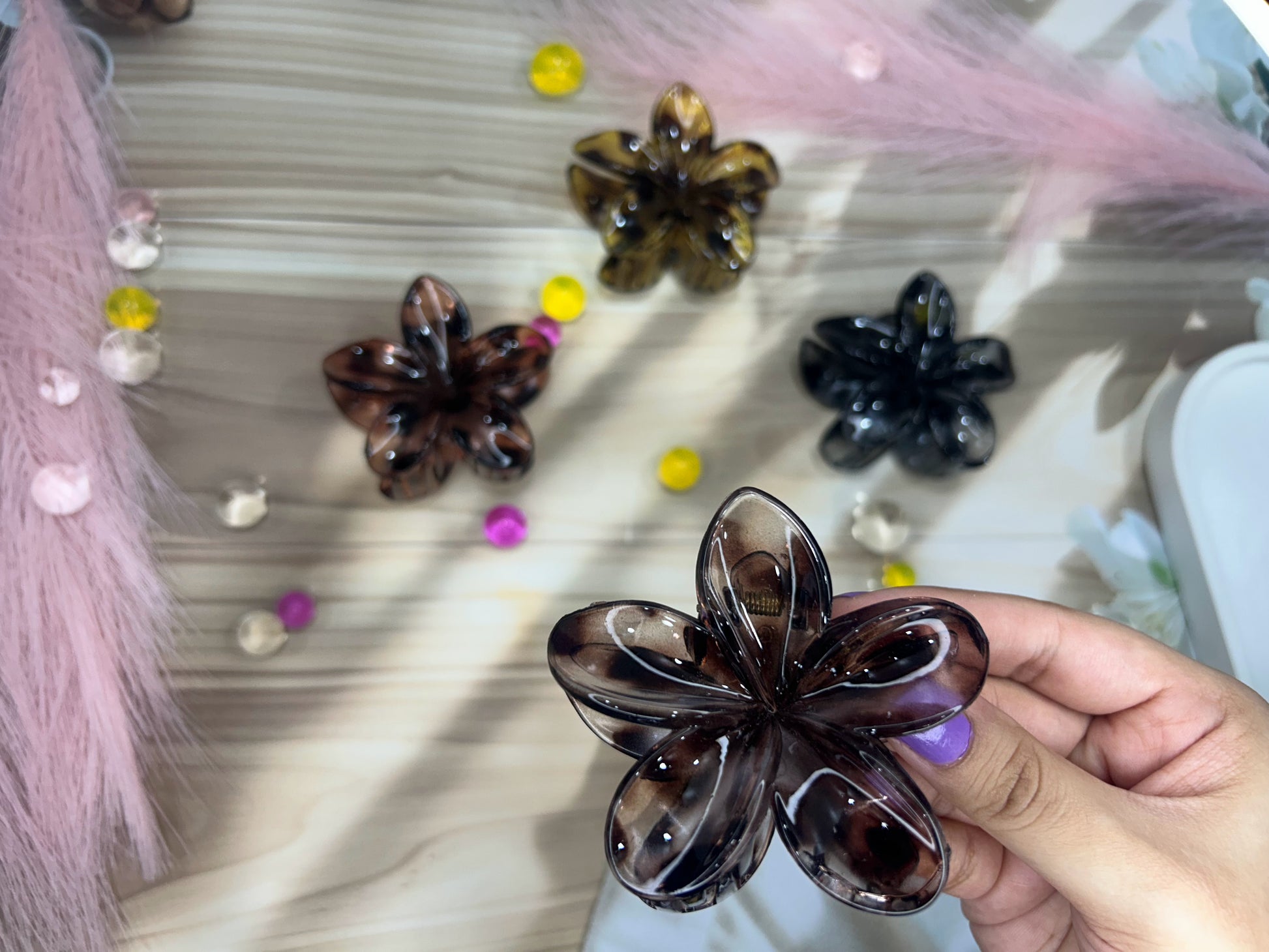 Hand holding a flower-shaped hair clip with blurred decorative background