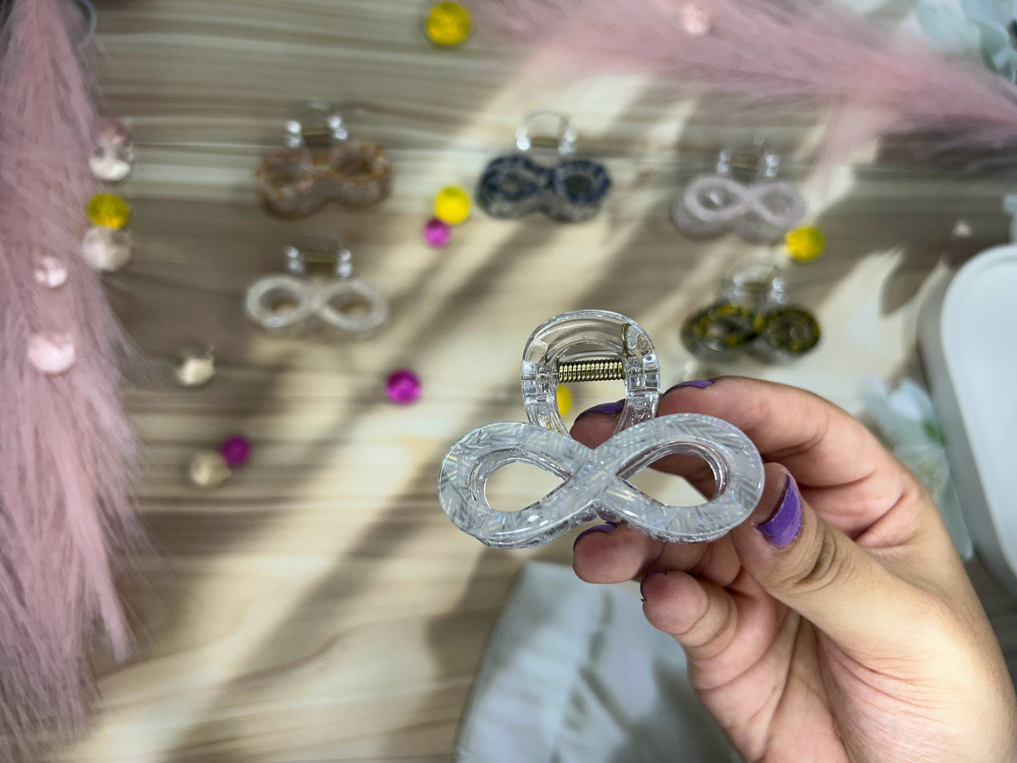 Hand holding a crystal infinity symbol earring with a blurred background of more earrings.