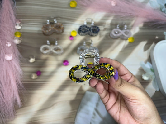 Hand holding a yellow and black patterned hair clip with earrings displayed in the background.