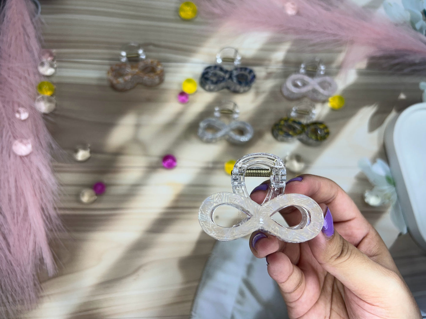 Hand holding a hair clip with a blurred background of more hair clips and decorations.