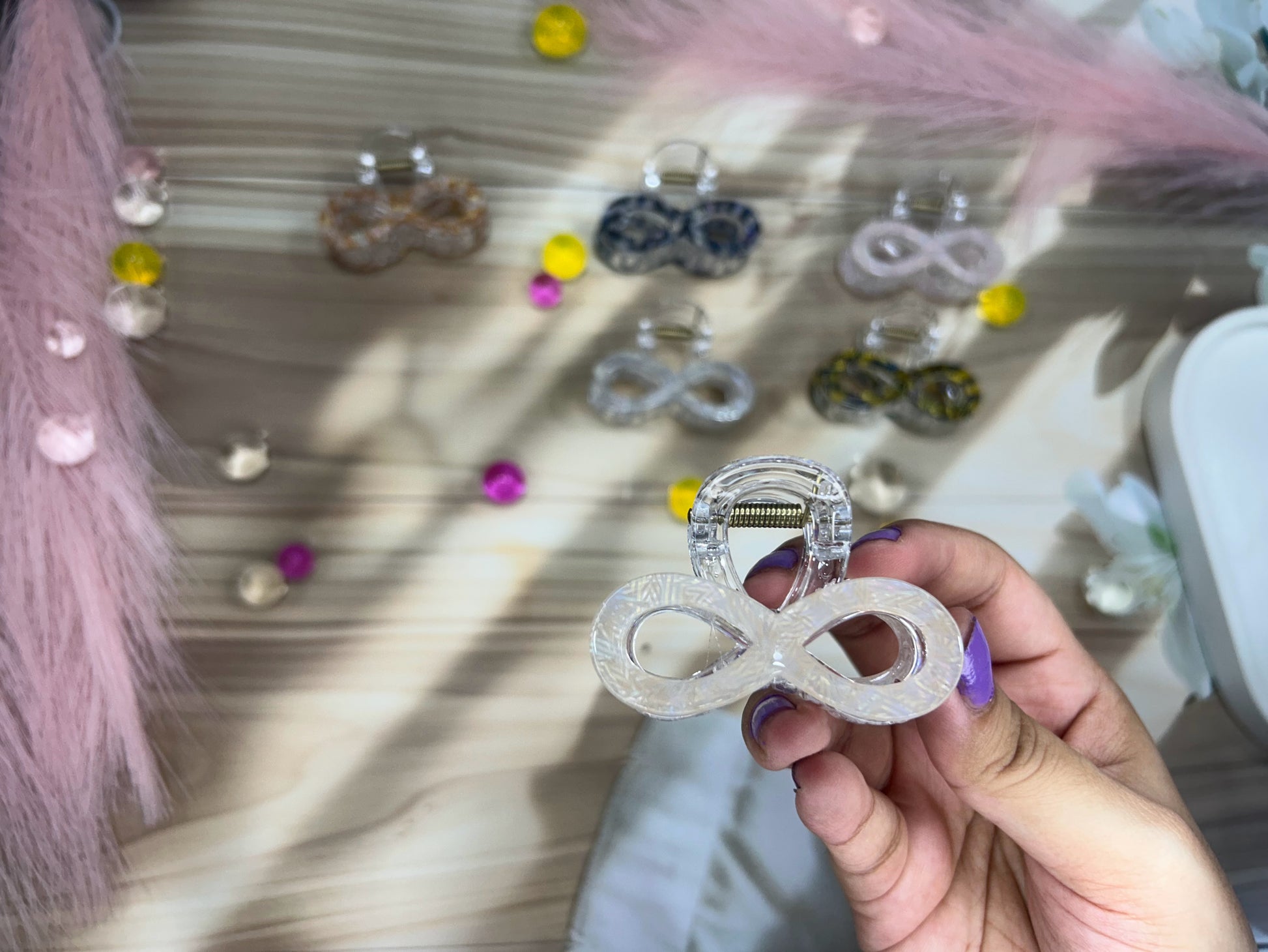Hand holding a hair clip with a blurred background of more hair clips and decorations.