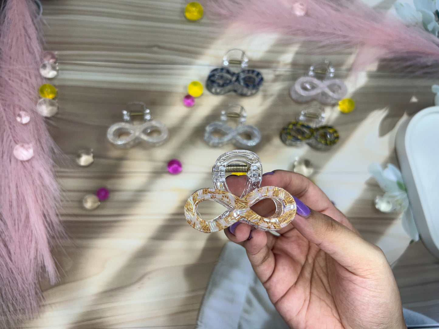 Hand holding a decorative hair clip with an infinity symbol in front of a display of similar clips.