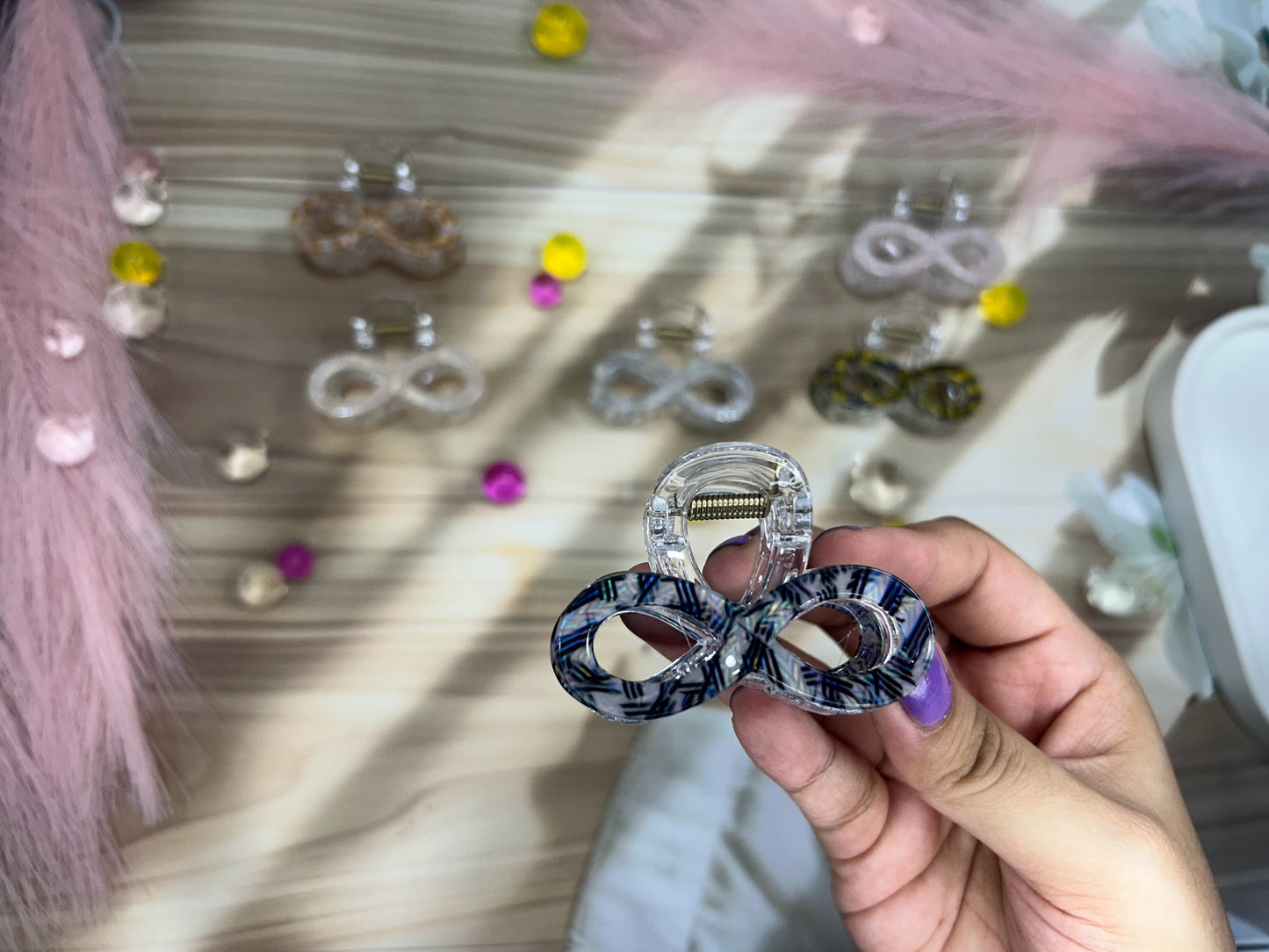 Hand holding a clear earring with blue and black pattern against a background of various earrings.