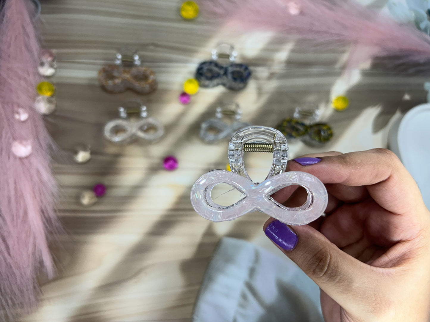 Hand holding a clear hair clip with infinity symbol against a background 