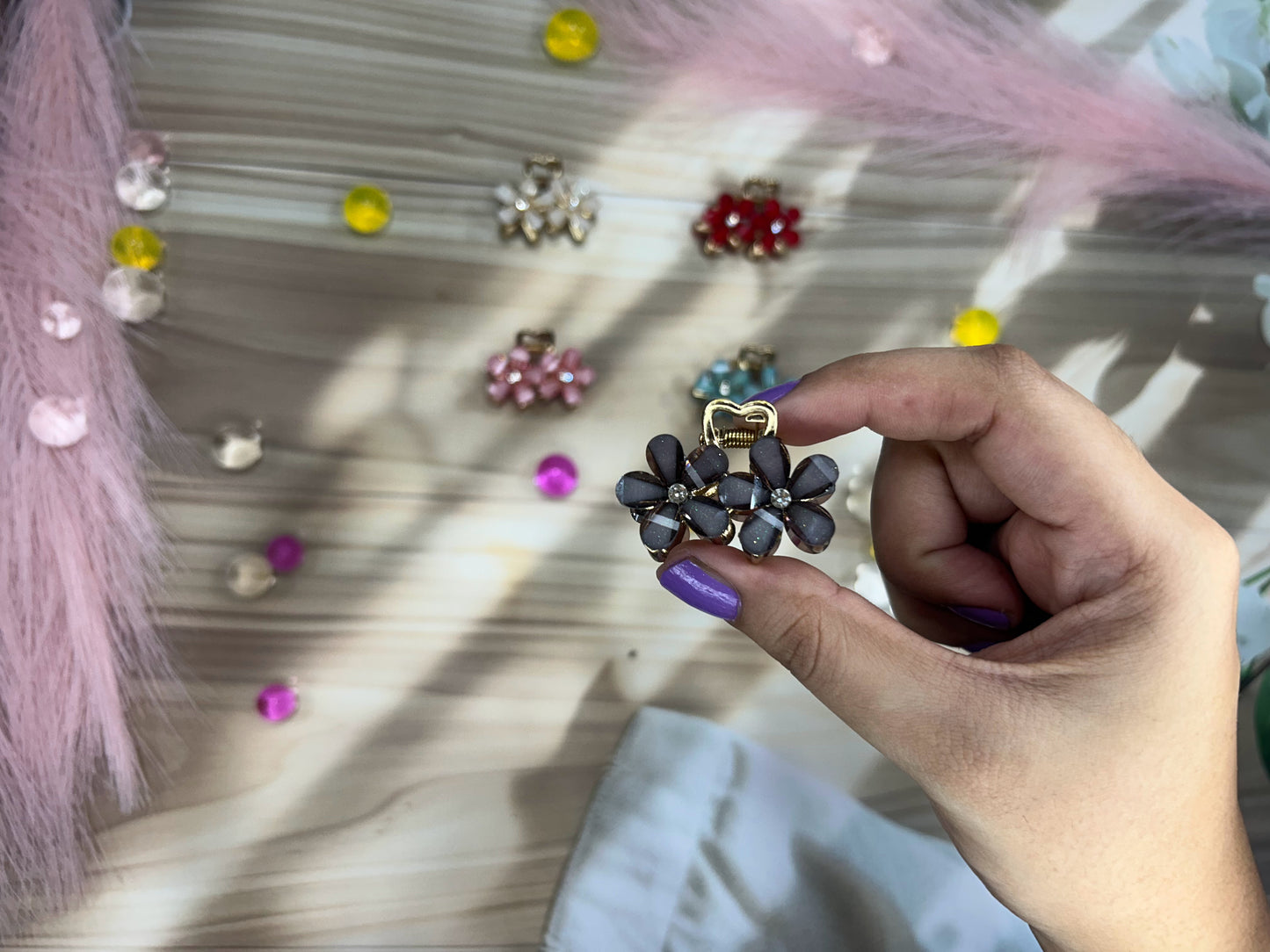 Hand holding a floral hair clip with colorful earrings in the background
