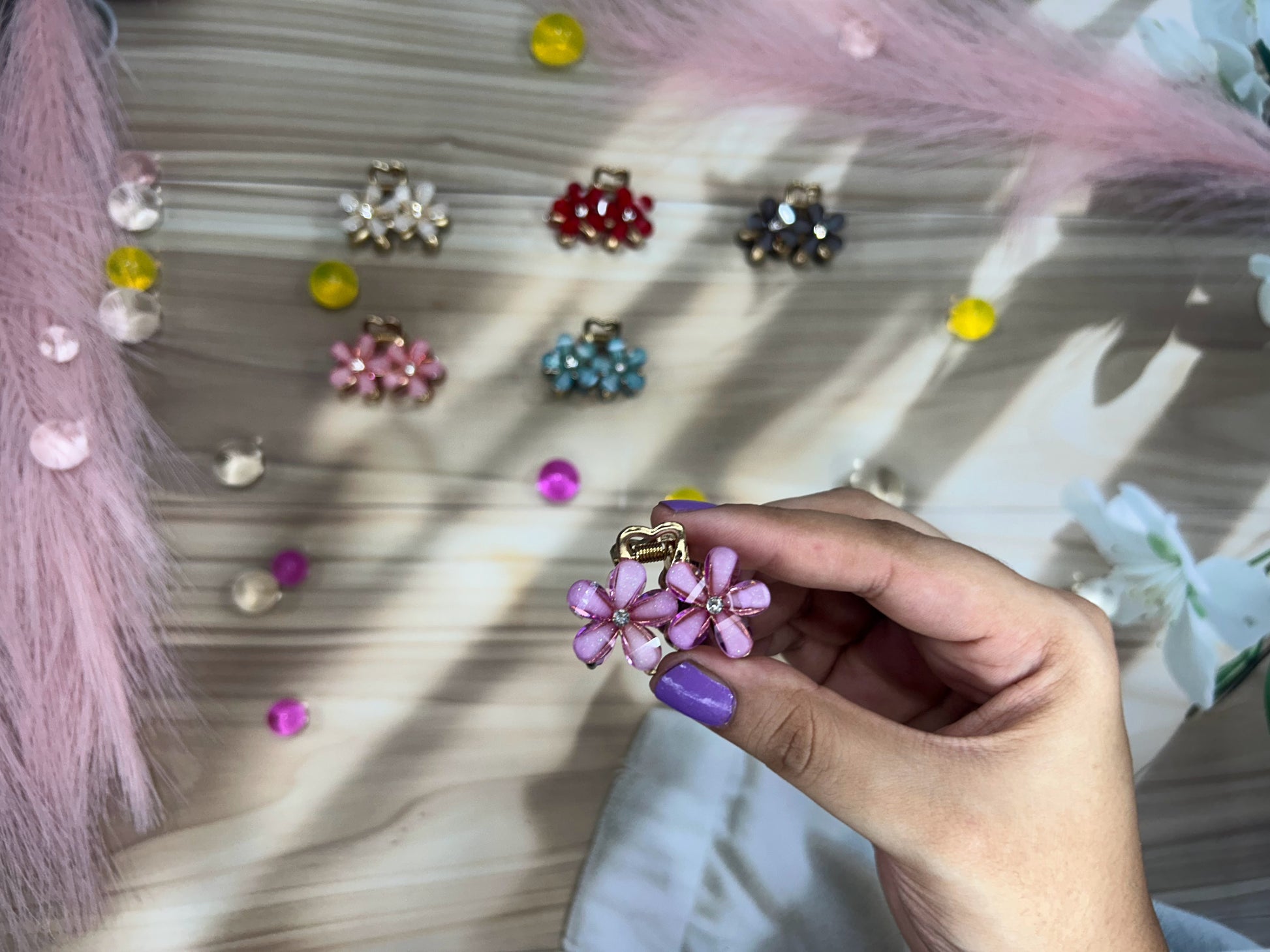 Hand holding a pink floral hair clip with colorful clips in the background on a textured surface.