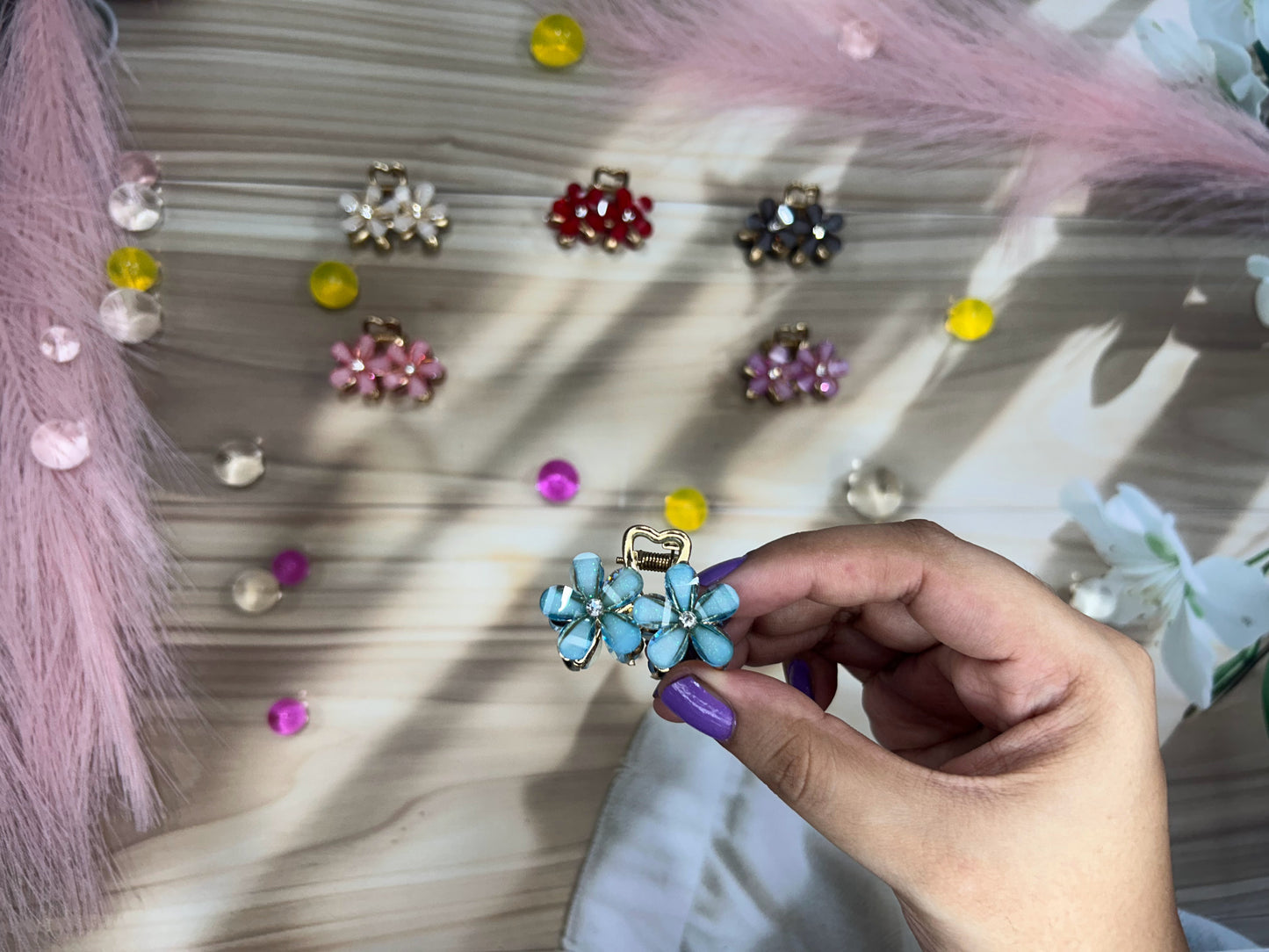 Hand holding a blue floral hair clip with colorful earrings on a textured surface
