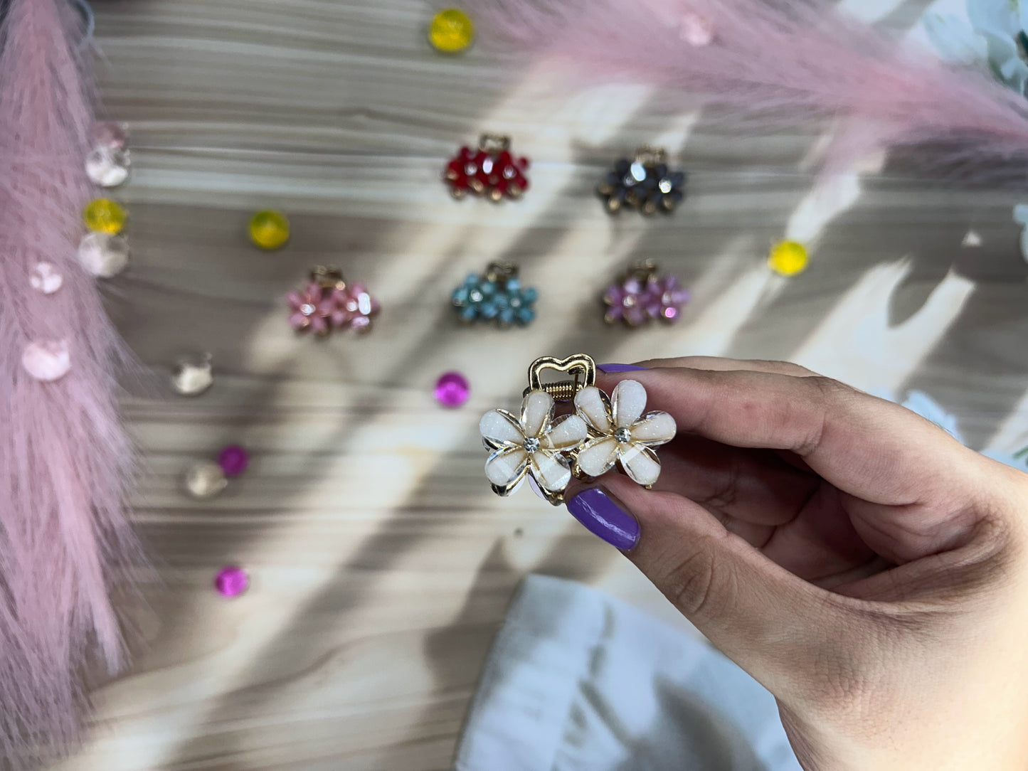 Hand holding a decorative hair clip with colorful earrings in the background