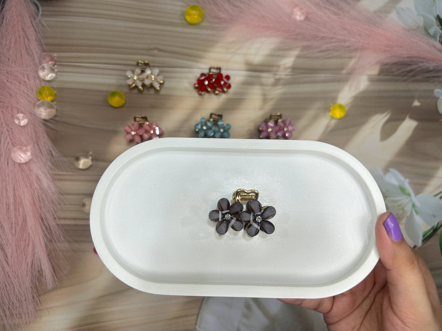 Floral earrings in a white case held by a hand with purple nail polish, with colorful earrings in the background.