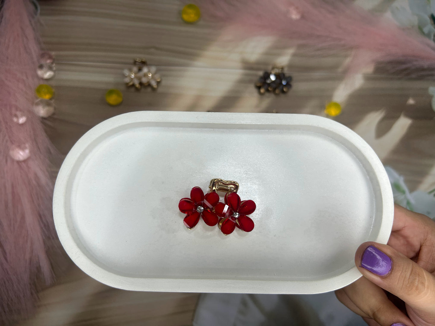 Red floral earring on a white tray held by a hand with purple nail polish.