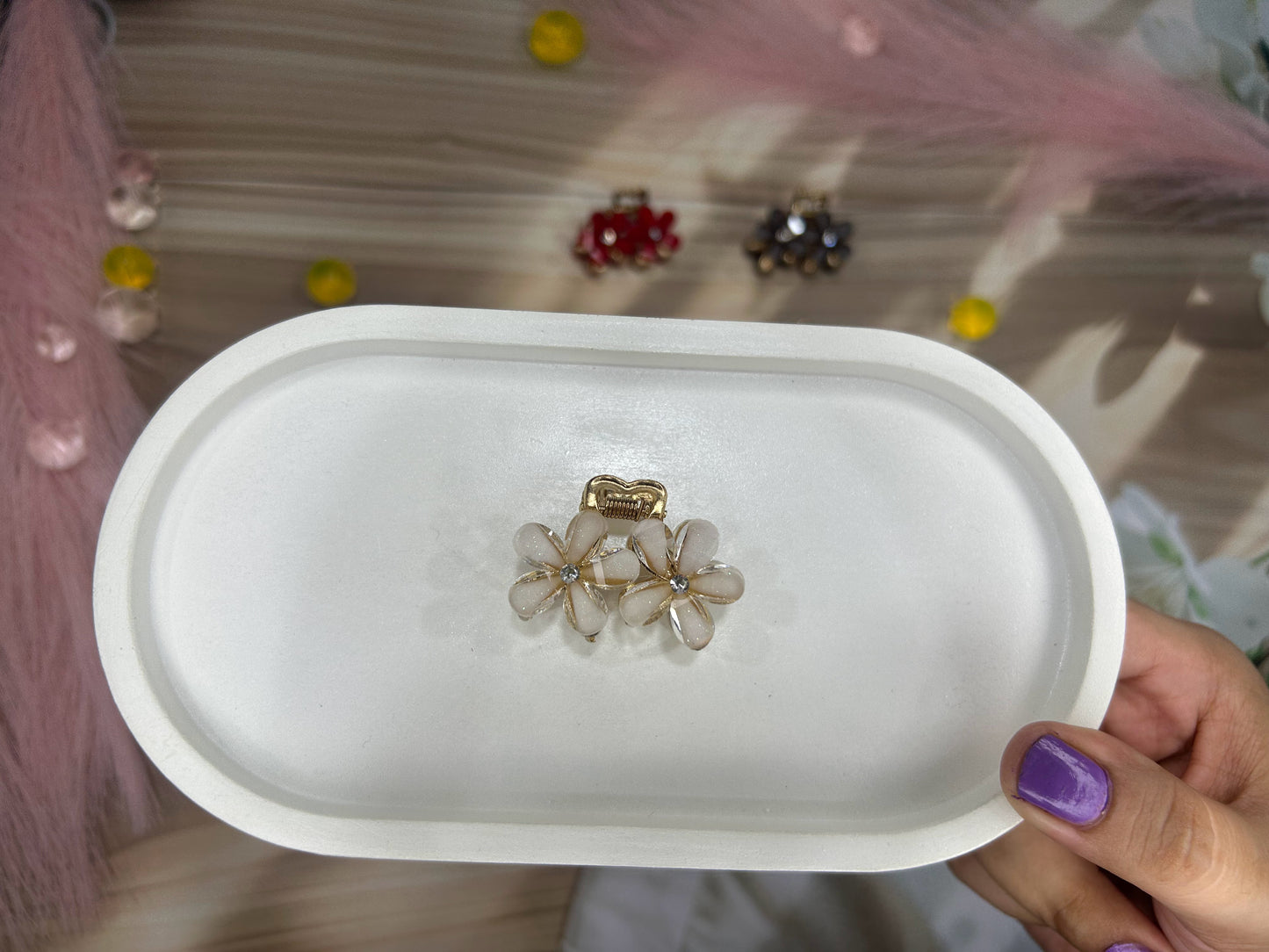 Hand holding a white dish with a floral earring on a blurred background
