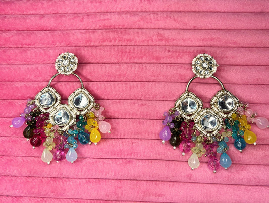 Colorful earrings with gemstones on a pink wooden background