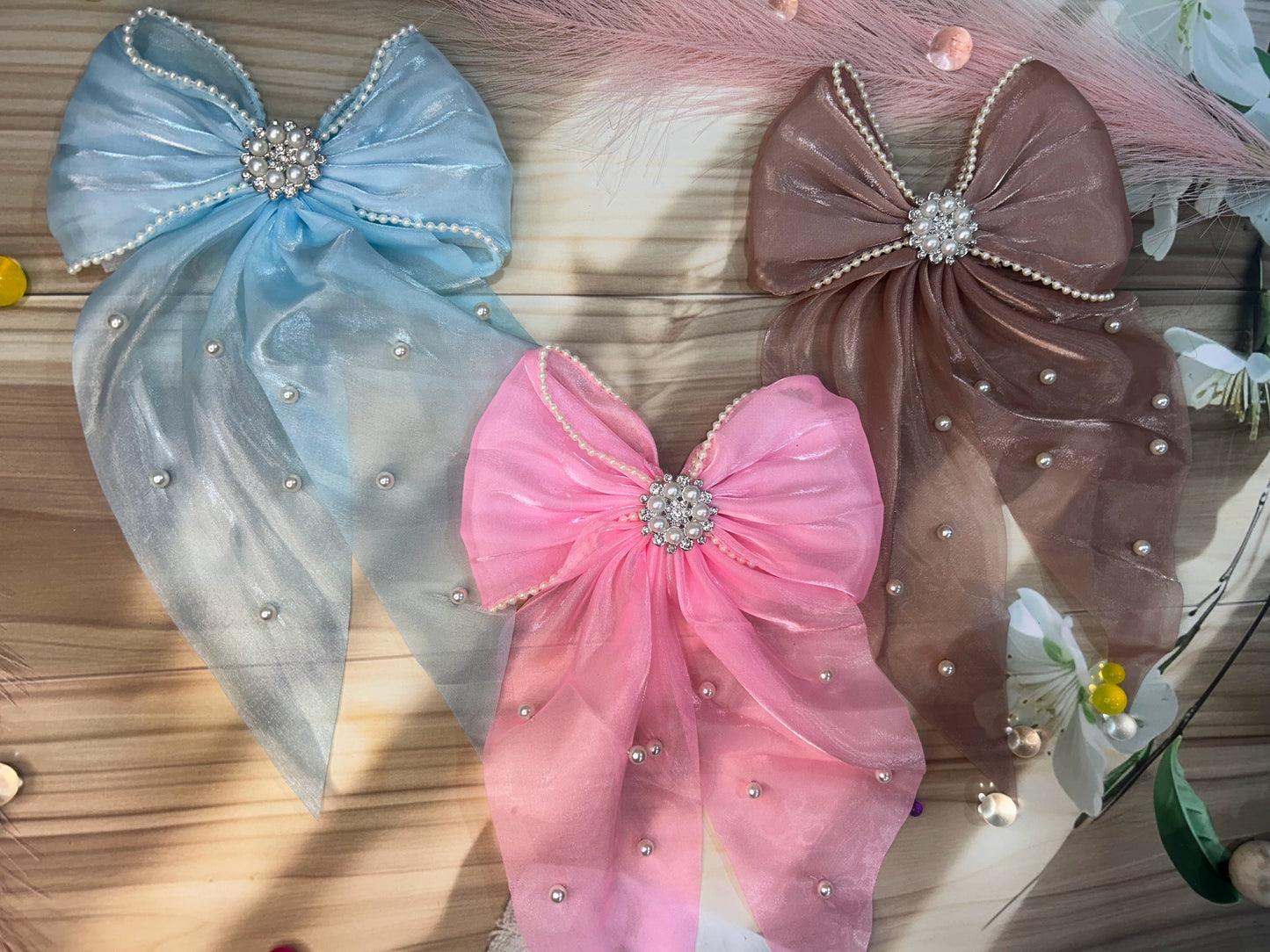 Three decorative bows in blue, pink, and brown with rhinestone centers on a wooden surface.