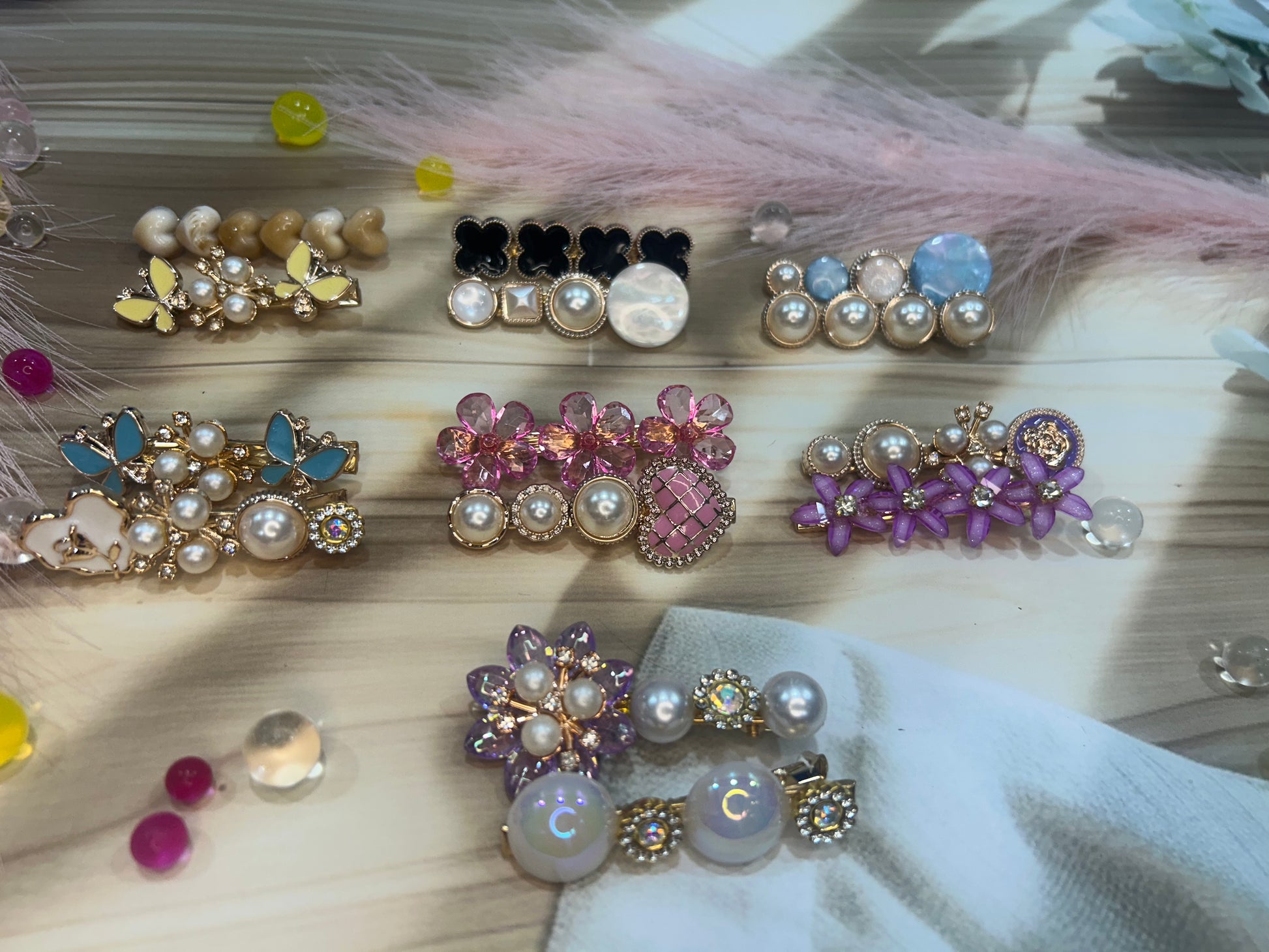 Collection of decorative hair clips with pearls and gemstones on a textured surface.