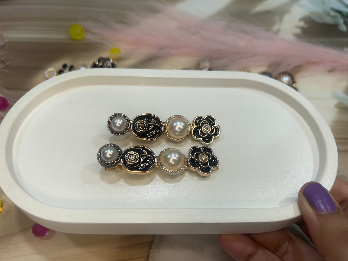 Set of floral hair clip on a white tray held by a hand with purple nail polish.