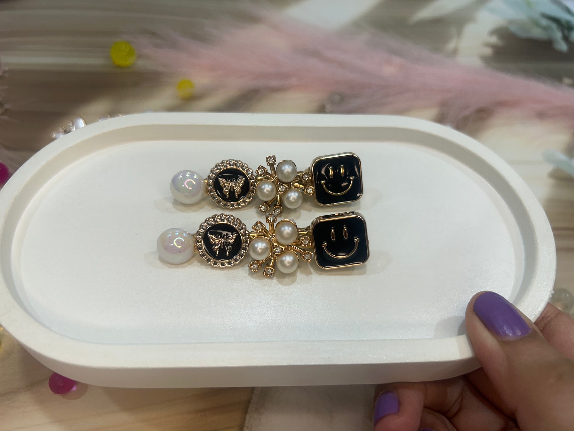 Pair of hair clip with smiley face design on a white tray held by a hand.