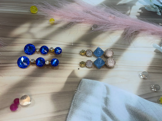 Pair of blue and gold hair clip on a wooden surface with loose gemstones.