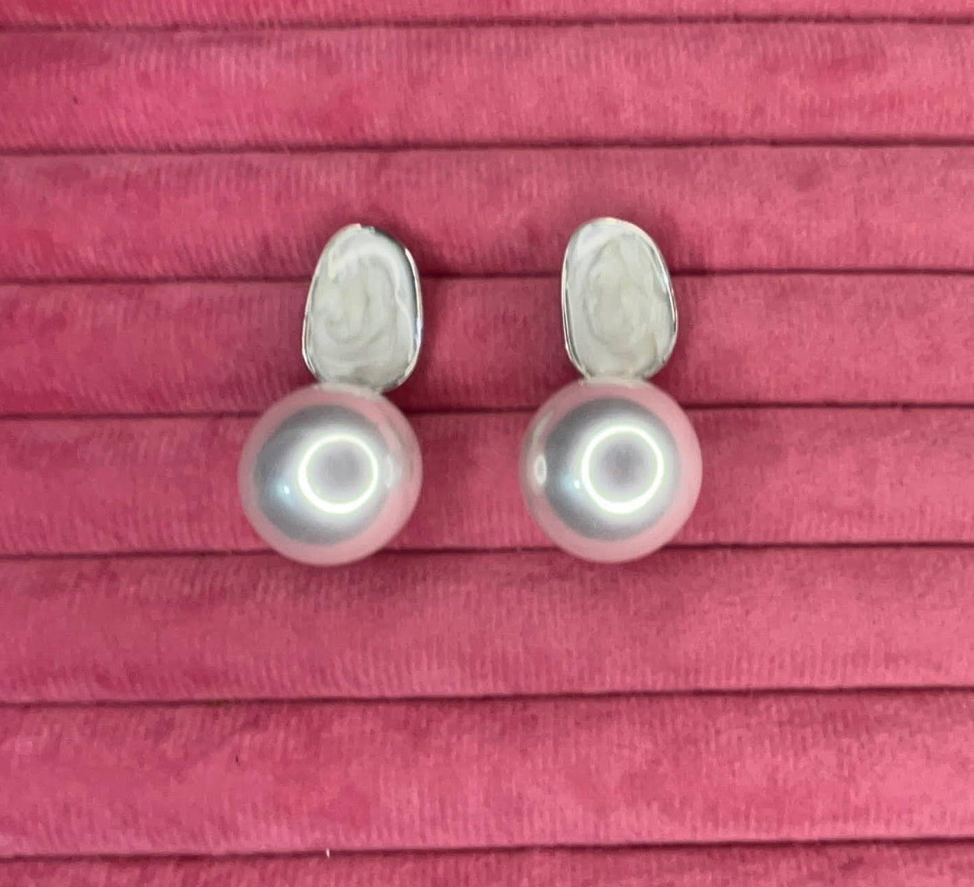 Pair of pearl earrings in their box on a pink wooden surface