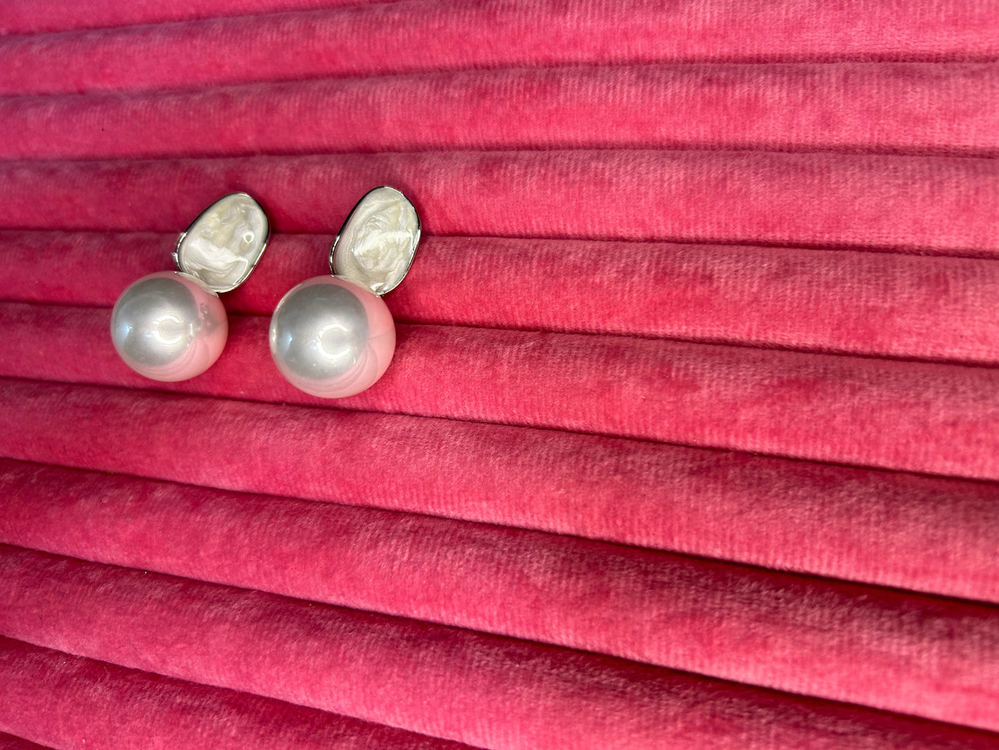 Pearl earrings on a pink pleated fabric background