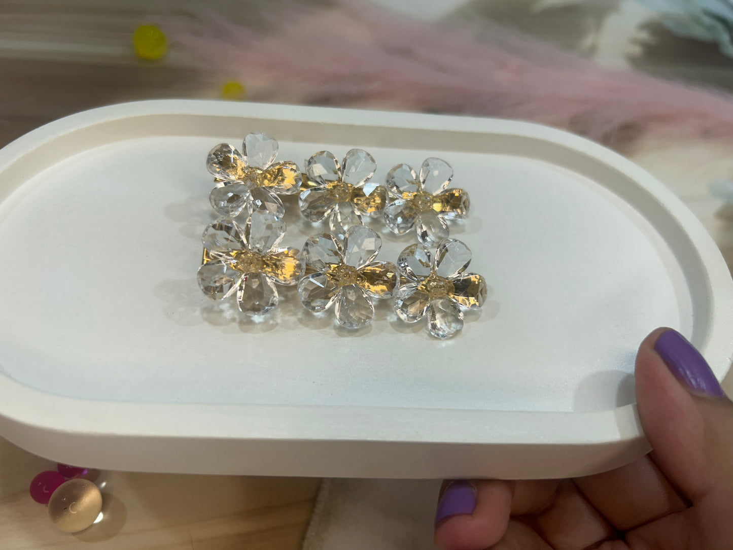 Clear crystal hair clip with gold accents on a white tray held by a hand.
