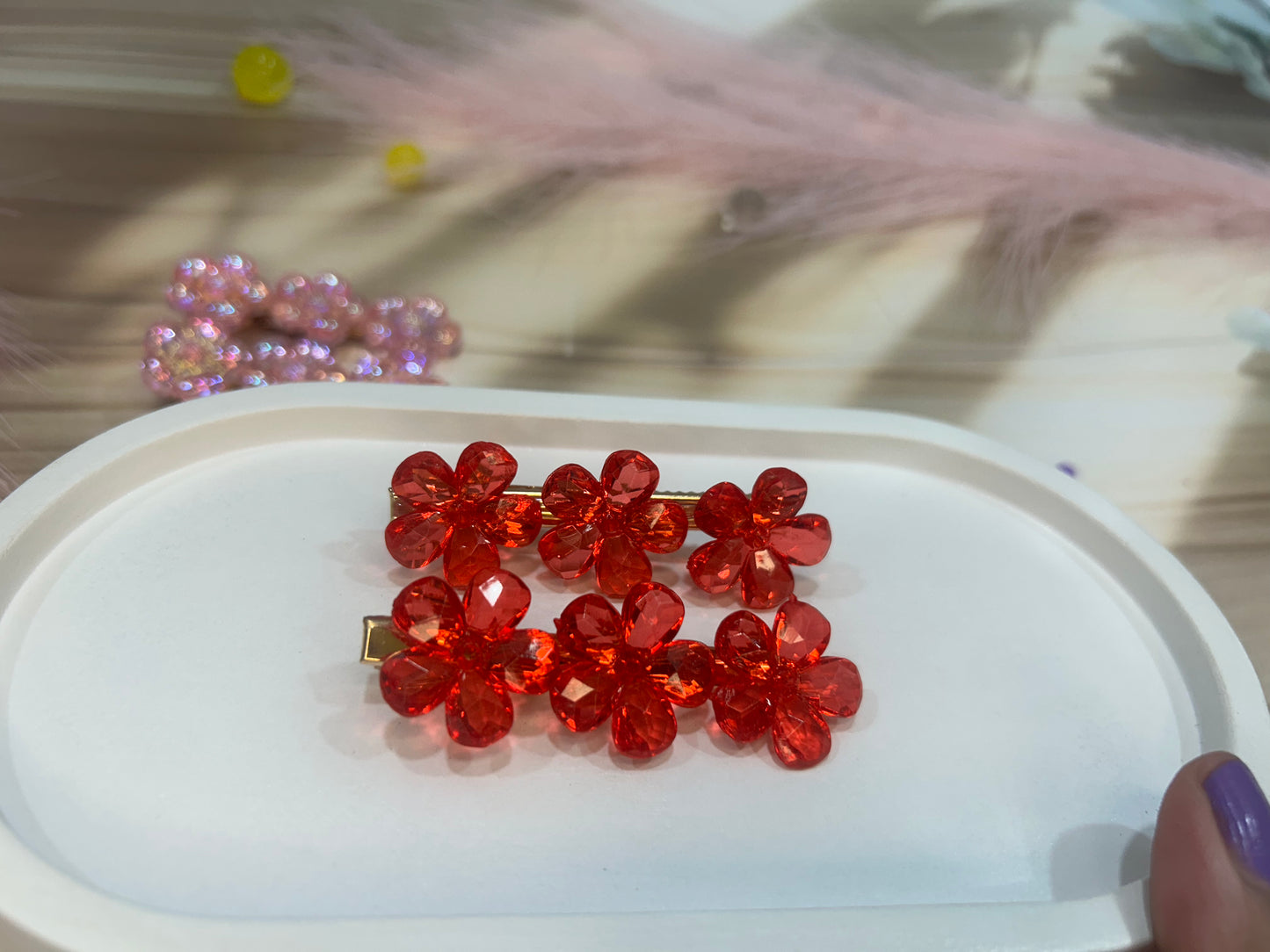 Red floral hair clip on a white surface with blurred background