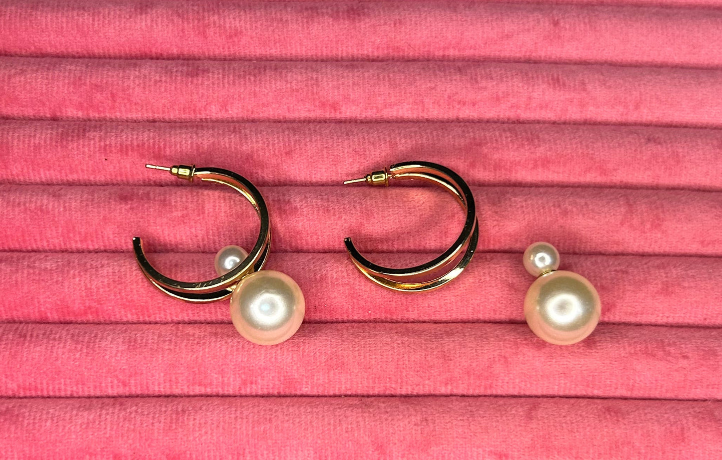 Pair of gold earrings with pearl accents on a pink textured surface