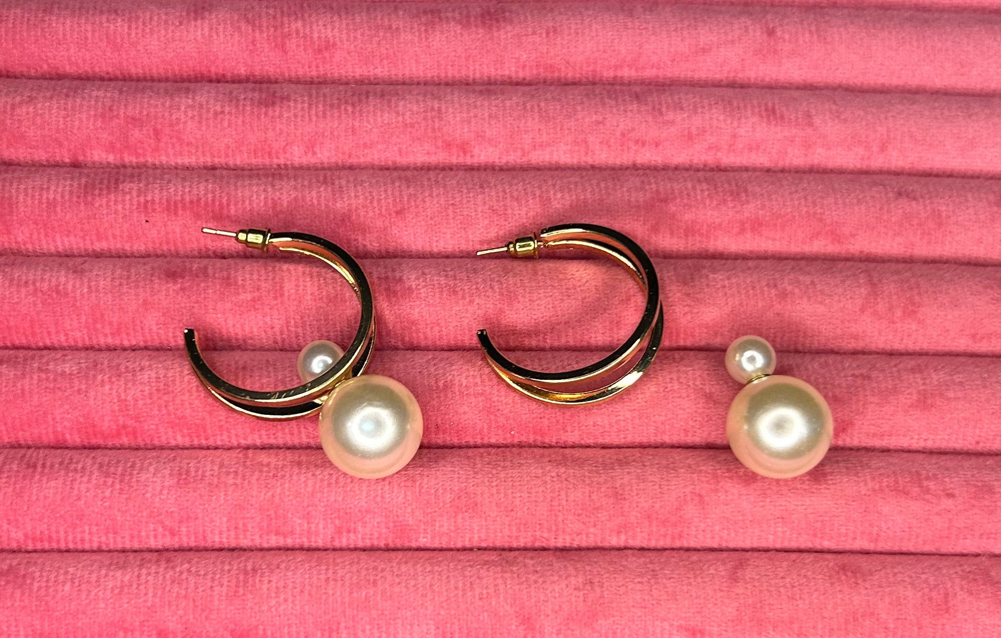 Pair of gold earrings with pearl accents on a pink textured surface
