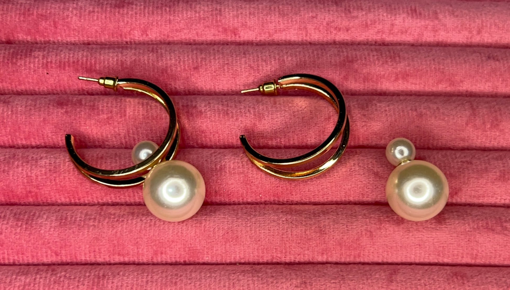Gold hoop earrings with pearls on a pink textured background